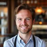 Professional headshot of Tom, Cafe Manager, smiling in front of a coffee counter